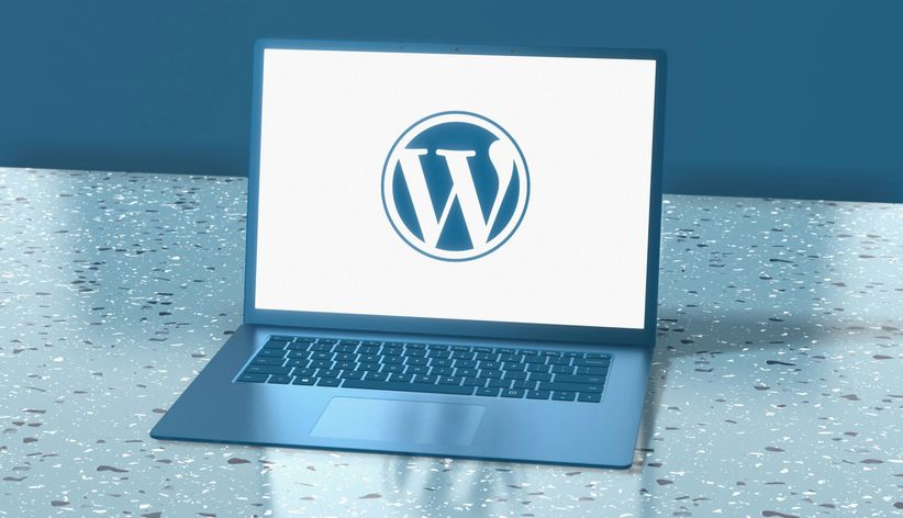 A laptop sitting on a table with a wordpress logo on the screen.