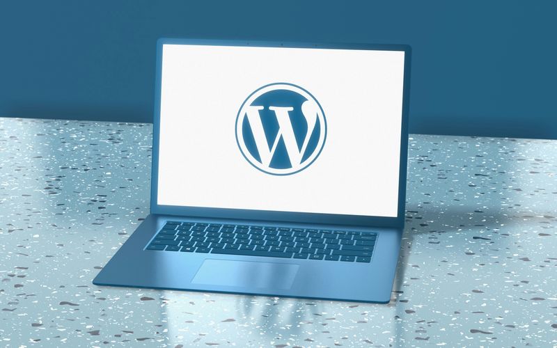 A laptop sitting on a table with a wordpress logo on the screen.